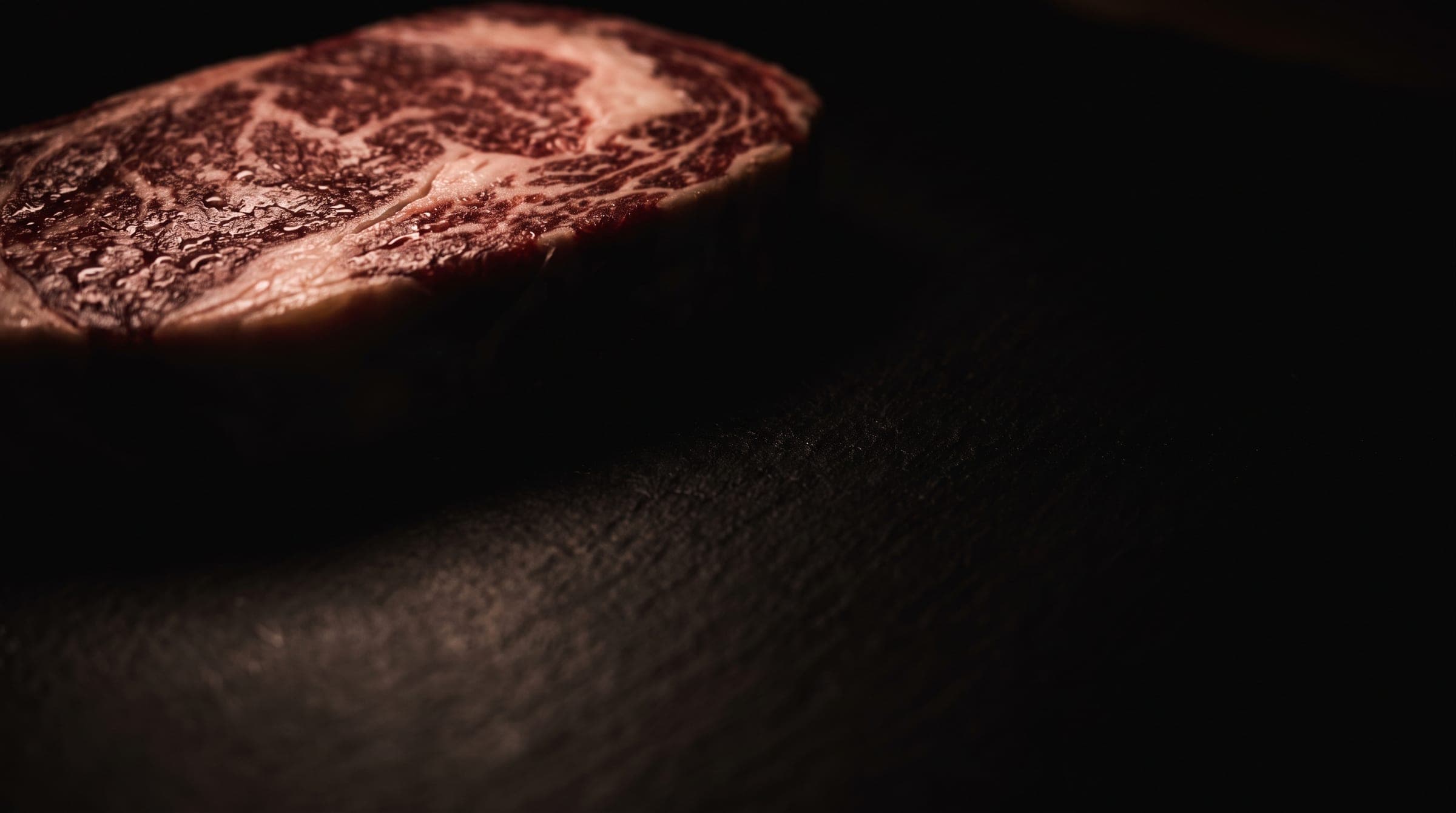 Raw, heavily marbled steak on a dark stone slab
